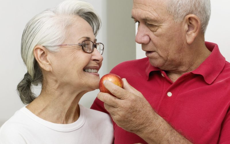 Senior man offering senior woman a nectarine, close-up